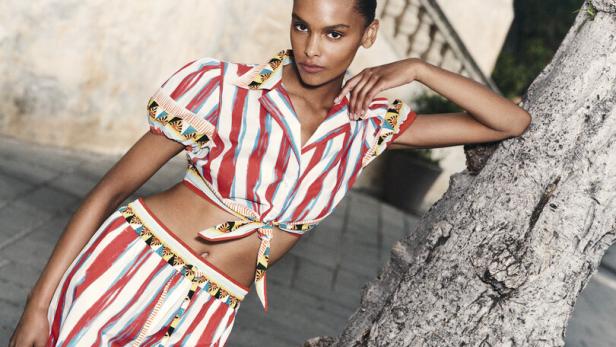 Eine Frau in einem gestreiften Sommeroutfit lehnt an einem Baum.