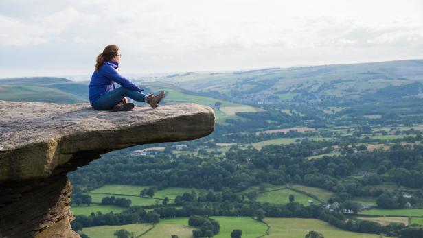 Eine Frau sitzt auf einem Felsen im Hope Valley im Peak District.