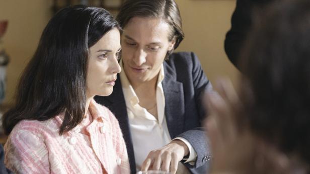 Eine Frau in einer rosa Jacke sitzt mit einem Mann am Tisch.