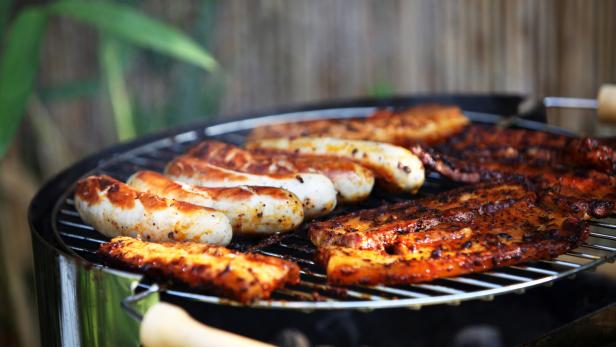Auf einem Grill liegen Würstchen und mariniertes Fleisch.