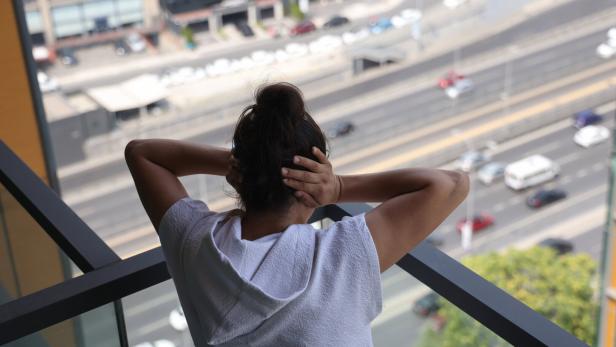 Eine Frau steht auf einem Balkon, blickt auf eine verkehrsreiche Straße und hält sich die Ohren zu: Stress ist eine der Ursachen für Entzündungsprozesse im Körper.