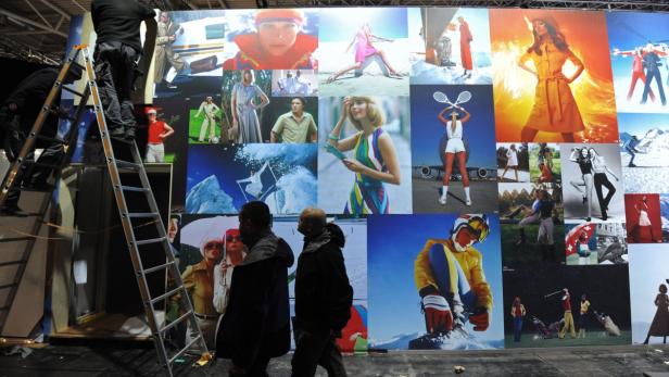 Mitarbeiter montieren eine Wand mit Modefotografien aus verschiedenen Jahrzehnten.