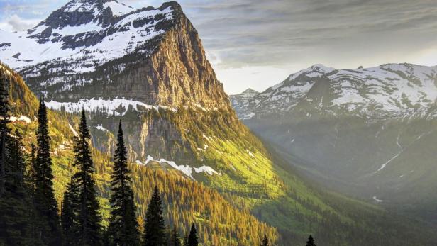 Ein Bergmassiv mit schneebedeckten Gipfeln und grünen Tälern im Sonnenlicht.