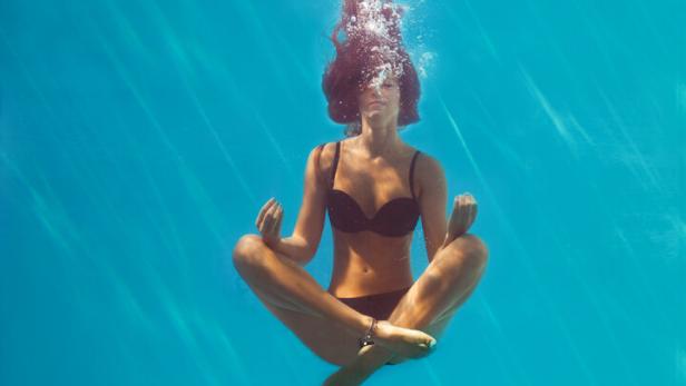 Frau schwebt in Yogaposition in einem Pool unter Wasser