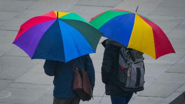 Zwei Personen mit bunten Regenschirmen gehen im Regen.
