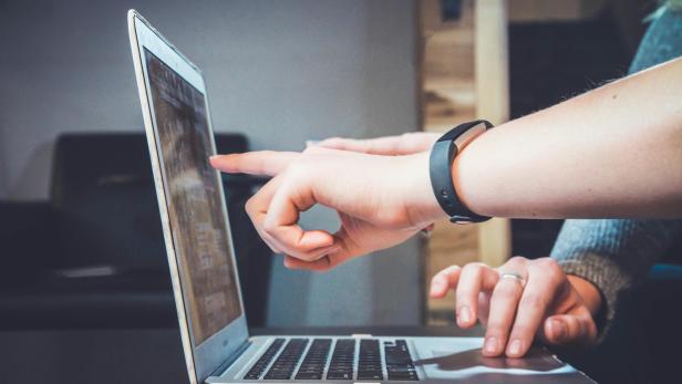 Zwei Personen zeigen mit dem Finger auf einen Laptop