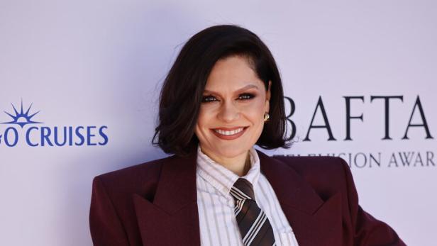 Jessie J posiert in einem burgunderfarbenen Hosenanzug auf einer Preisverleihung.