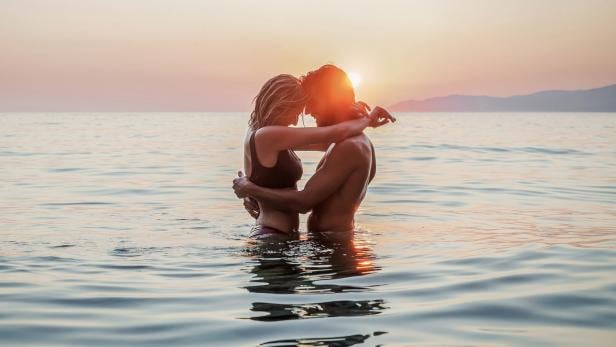 Ein Paar umarmt sich im Wasser bei Sonnenuntergang.