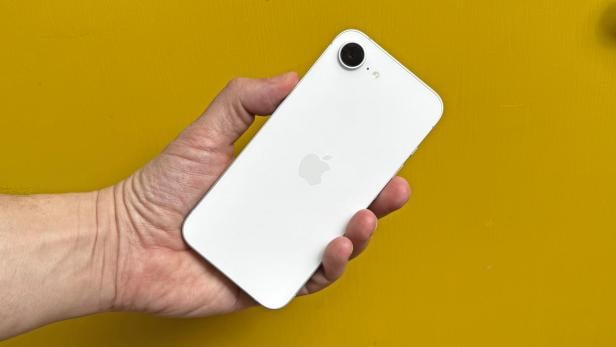 Eine Hand hält ein weißes iPhone 16e.