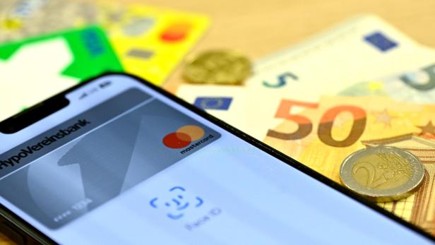 Ein Smartphone mit einer HypoVereinsbank-Mastercard-App liegt auf Euroscheinen und Münzen.