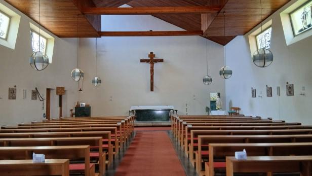 Kircheninnenraum mit Holzbänken, Mittelgang, Altar und Kreuz an der Frontwand.