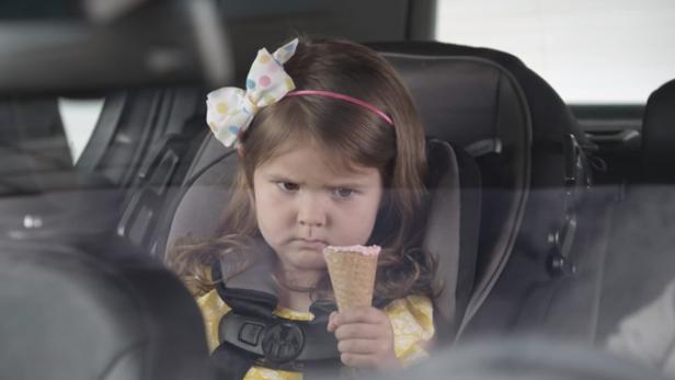 Ein mürrisches kleines Mädchen sitzt im Autositz und hält ein Eis in der Hand.