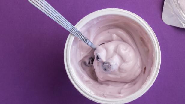 Joghurtbecher mit Heidelbeerjoghurt, Löffel und Deckel.