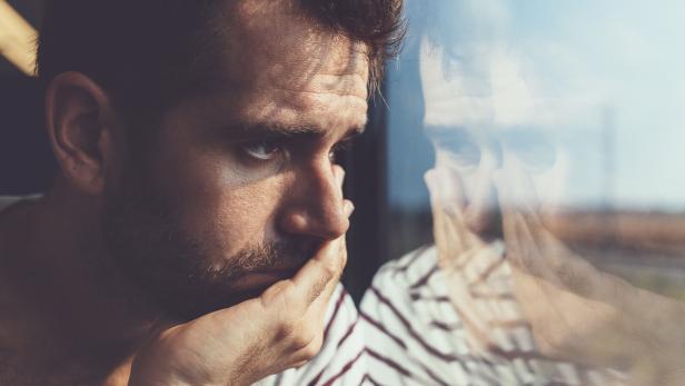 Sad young man looking through the window