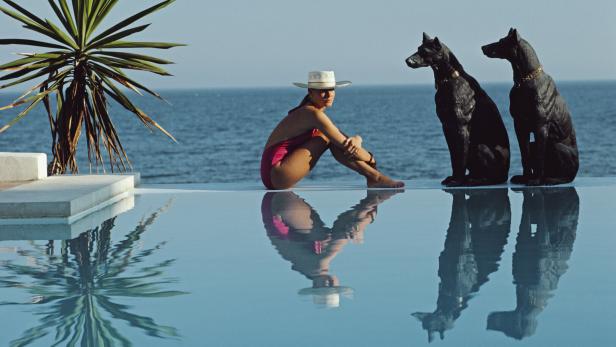 Eine Frau sitzt am Pool, hinter ihr liegt das weite Meer