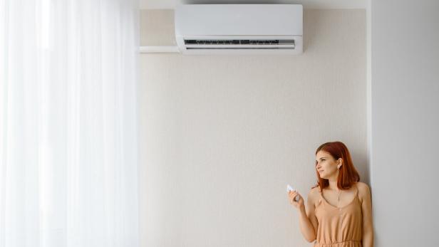 Young beautiful woman in her white apartment turns on the air conditioner and enjoys the cool.