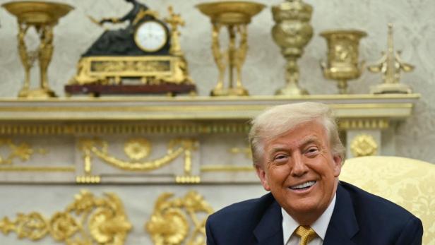 Trump lächelt, hinter ihm goldene Schmuckstücke.