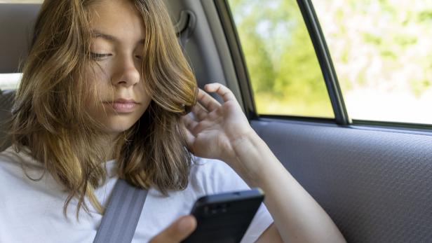 Teenager-Mädchen sitzt auf dem Rücksitz eines Autos und benutzt ein Smartphone.