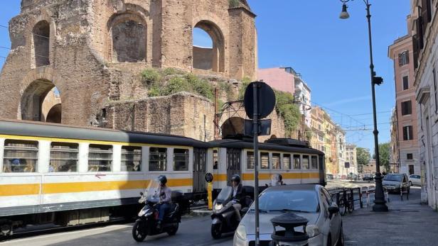 Eine Straße in Rom mit einer alten Ruine, einer Straßenbahn und Rollern.