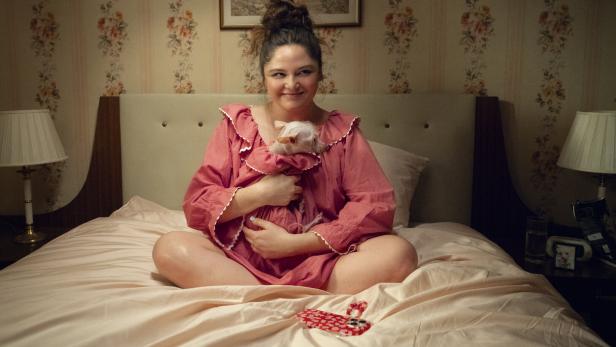 Eine Frau sitzt auf einem Bett und hält ein kleines, weißes Tier im Arm.