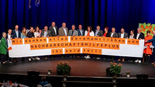 Nachbarschaftshilfe Plus: Vereinsmitglieder auf einer Bühne mit einem Transparent: Danke den Ehrenamtlichen, ihr seid toll