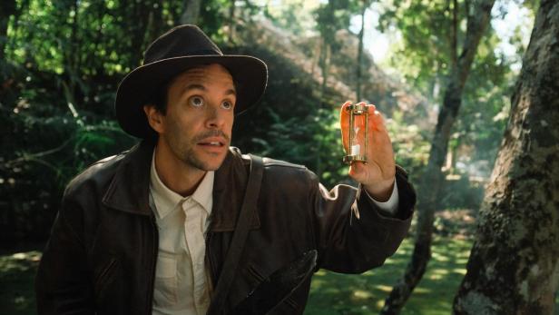 Ein Mann im Dschungel, der einen goldenen Stundenglas betrachtet.