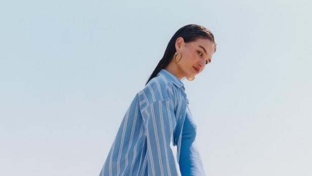 Eine Frau in Badebekleidung und einem blau-weiß gestreiften Hemd am Strand.