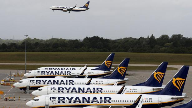 Mehrere geparkte Ryanair-Flugzeuge und ein startendes Flugzeug im Hintergrund.