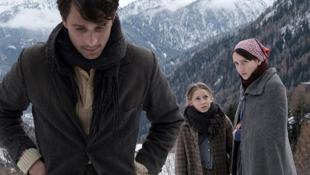 Ein Mann, ein Mädchen und eine Frau stehen in einer verschneiten Berglandschaft.