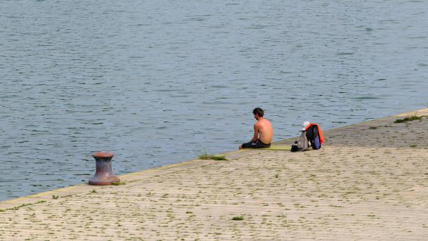 Mann sitzt an Ufer neben Wasser