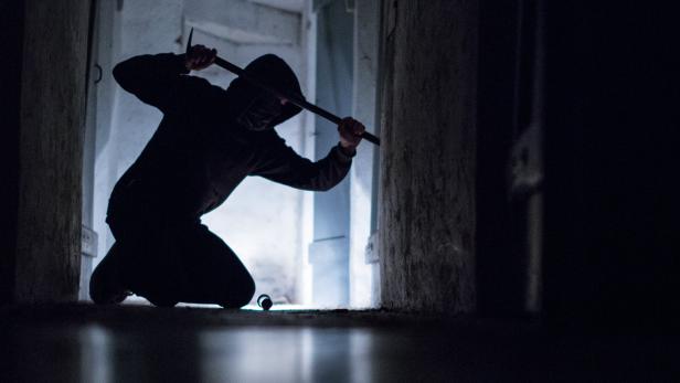 Einbrecher mit Brecheisen in einem dunklen Raum.