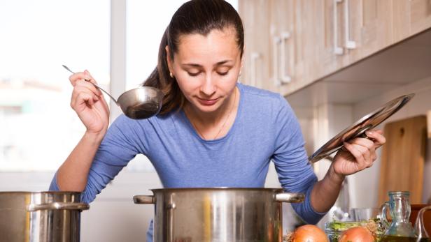 Warum wir nach dem Kochen oft keinen Hunger mehr haben Junge Frau kocht und schaut in den Topf