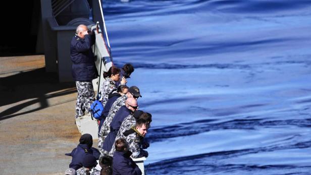 Eine Gruppe von Marineangehörigen blickt von einem Schiff auf das Meer.