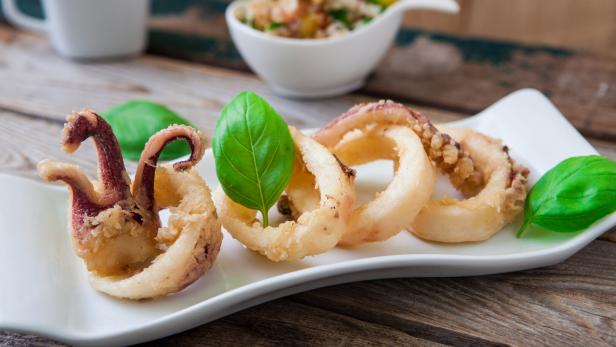 Frittierte Calamari-Ringe mit Basilikum auf einem weißen Teller.