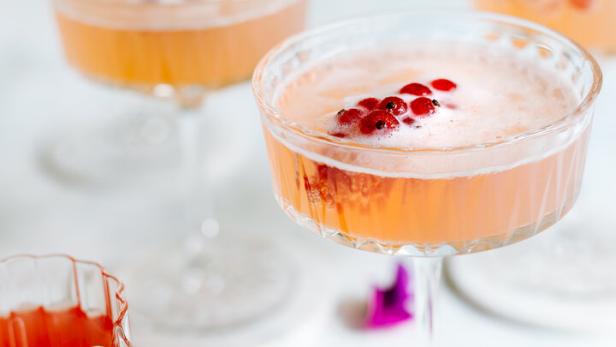 Mehrere Gläser mit einem rosa Getränk und roten Johannisbeeren stehen auf einem Tisch.