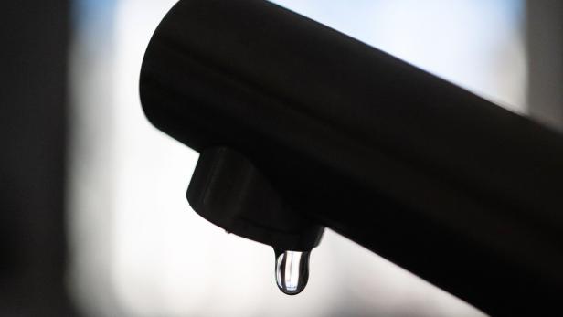 Ein einzelner Wassertropfen hängt an der Spitze eines dunklen Wasserhahns.