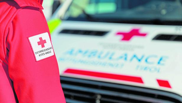 Ein Sanitäter steht mit dem Rücken zur Kamera vor einem Rettungsauto des Roten Kreuzes.