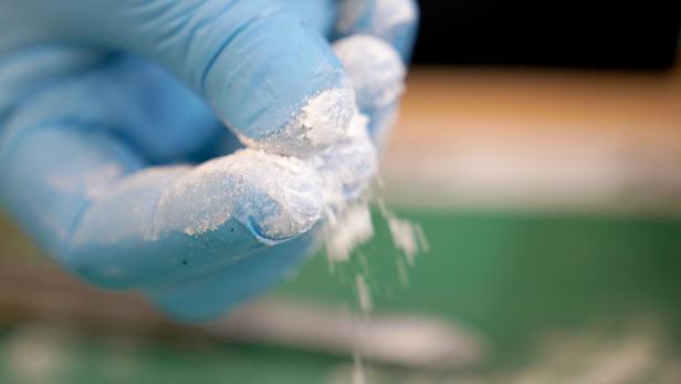 Eine Hand in einem blauen Handschuh rieselt weißes Pulver.