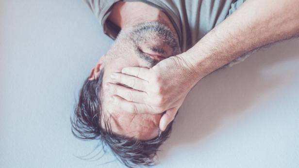 Mann liegt am Boden mit Hand vor dem Gesicht.