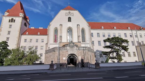 Große historische Klosteranlage mit rotem Dach und Torbogen vor blauem Himmel.