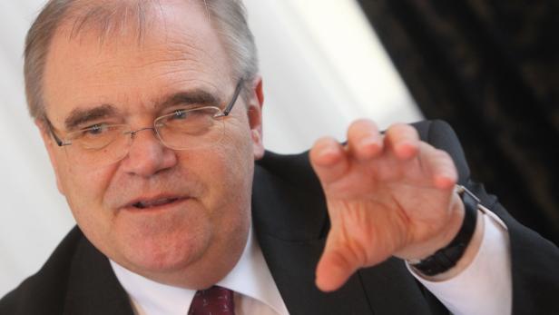 Ein Mann mit Brille und Anzug gestikuliert mit der Hand.