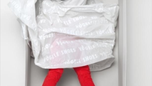Ein junger Mann liegt in einem Schuhkarton, bekleidet mit roter Hose und Schuhen der Marke Vögele Shoes.