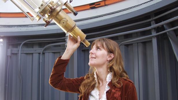 Eine Frau blickt durch ein goldenes Teleskop in einer Sternwarte.