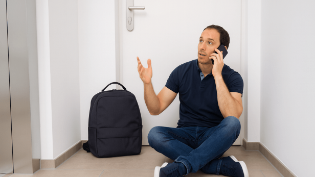 Ausgesperrter Mann sitzt ratlos vor Wohnungstür und telefoniert mit einem Schlüsseldienst.