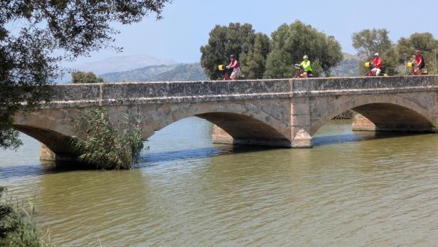 Eine Gruppe von Personen fährt mit Fahrrädern über eine Steinbrücke.