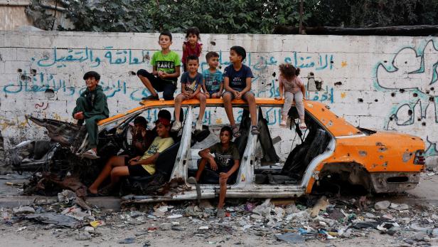 Palestinian children gather at a destroyed vehicle, in Khan Younis
