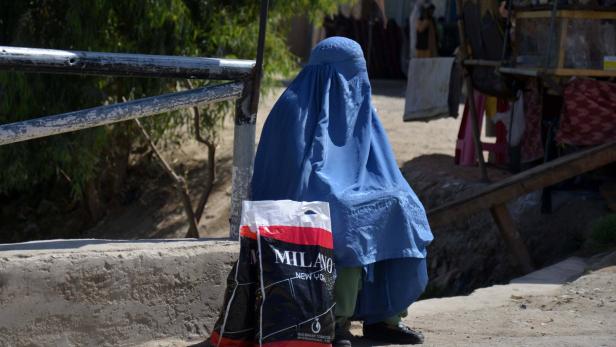 Eine Frau in blauer Burka sitzt neben einer "Milano"-Tasche auf einer Straße.
