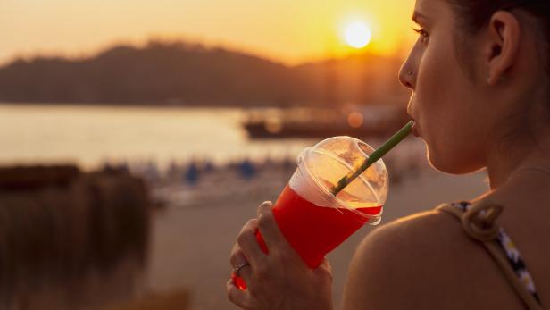Eine junge Frau schlürft genüsslich einen Slushie im Sonnenuntergang an einem Seeufer.
