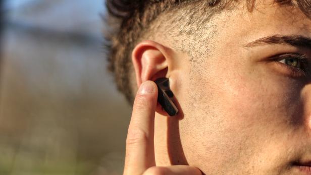 Ein junger Mann legt seinen Finger an seinen In-Ear-Kopfhörer