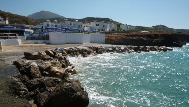 Küstenlandschaft mit türkisfarbenem Wasser und weißen Gebäuden im Hintergrund.